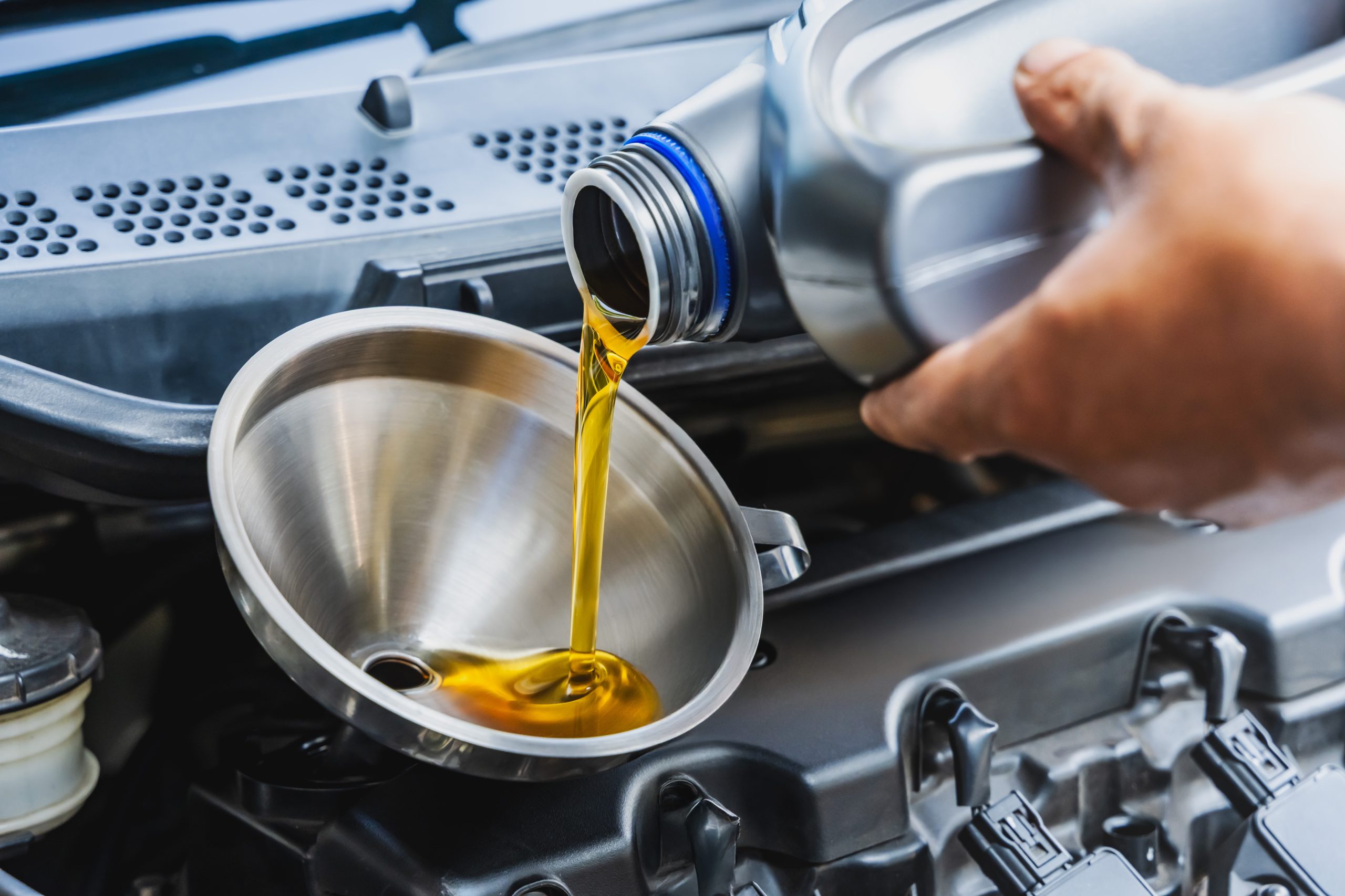 Close-up of a synthetic motor oil change being performed under the hood of a vehicle for auto repair keywords.